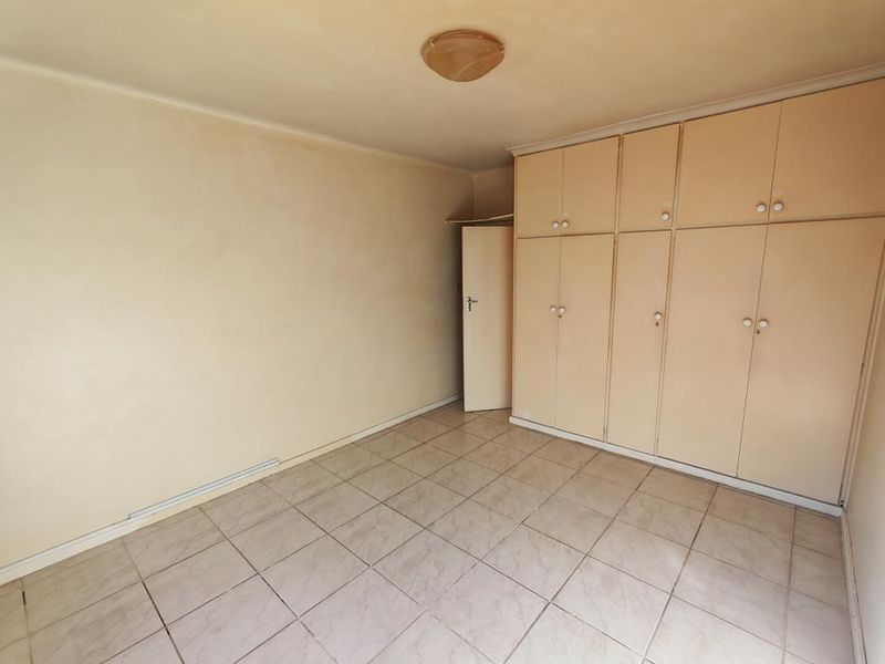 An empty bedroom featuring tiled flooring and extensive built-in cupboard storage, presenting a blank canvas for renovation or interior design updates.