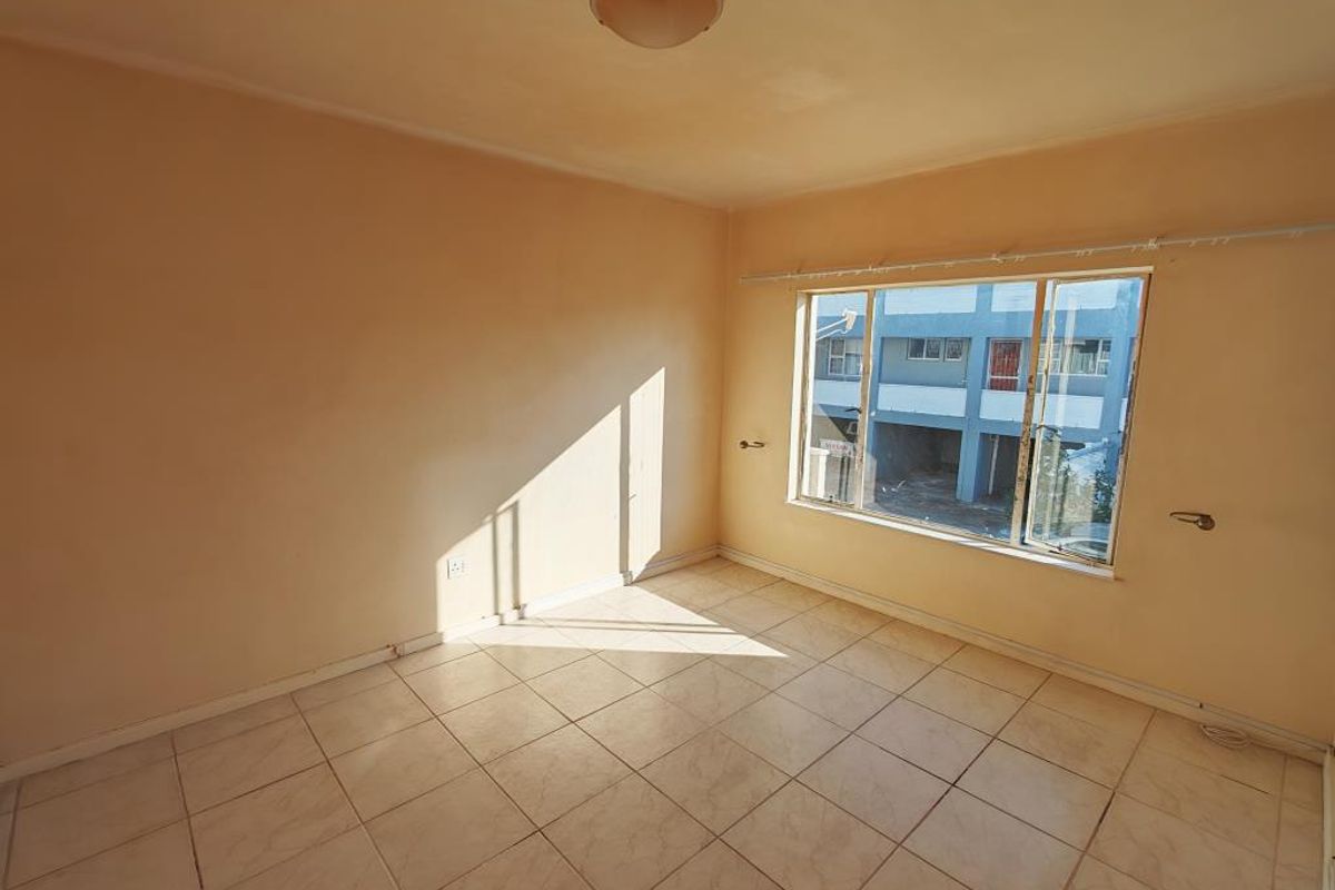 An empty bedroom featuring tiled flooring and a large sliding window, providing a blank canvas for personalization.