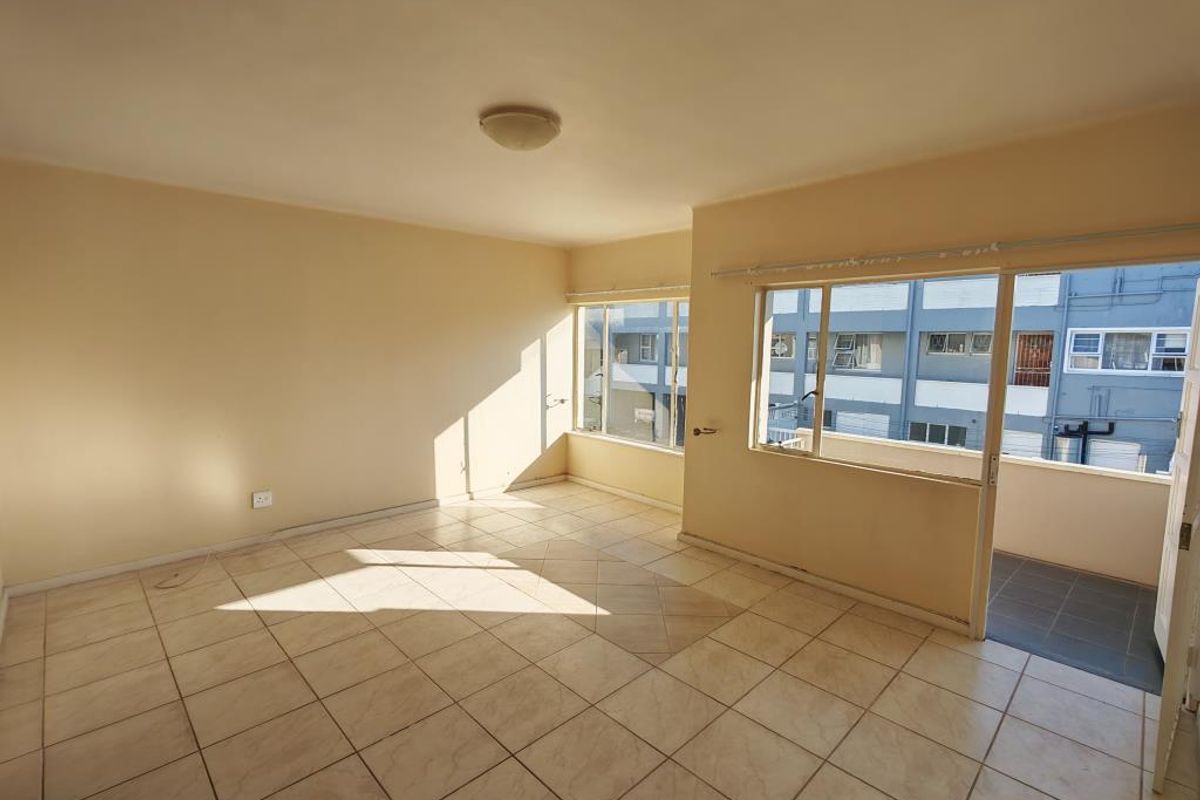 A bright, empty living room featuring tiled flooring and a sliding glass door leading to an outdoor balcony area.