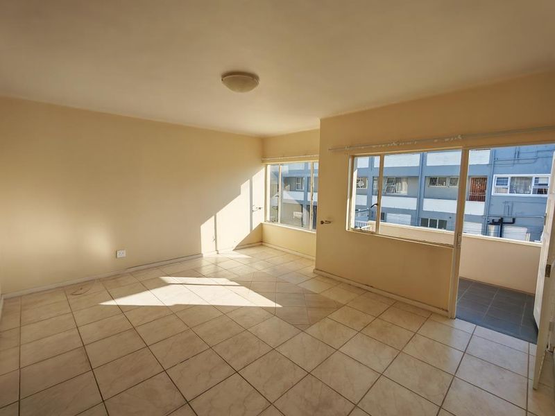 A bright, empty living room featuring tiled flooring and a sliding glass door leading to an outdoor balcony area.