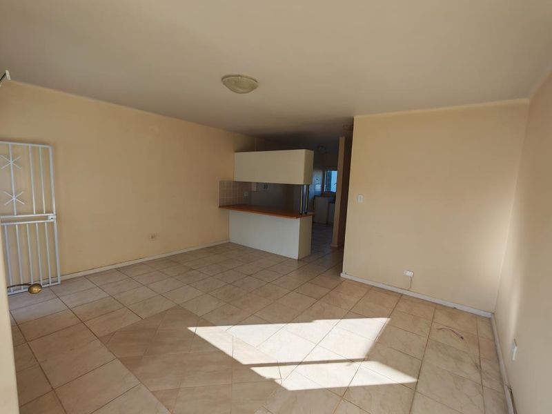 An open-plan living and kitchen area featuring tiled flooring, a breakfast bar, and neutral wall finishes, offering a blank canvas for renovation.