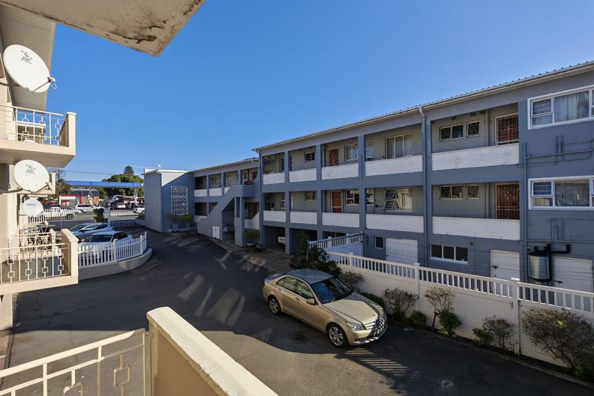 View of the apartment complex exterior, featuring a paved driveway, perimeter fencing, and balcony access with metal railings.