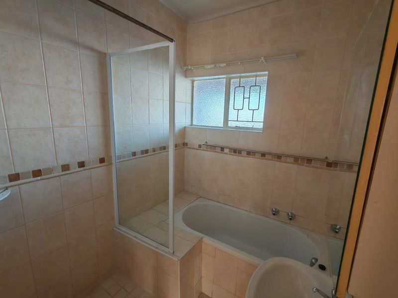 A functional bathroom featuring a built-in bathtub, glass shower screen, and neutral wall tiling, offering a clean and practical space.