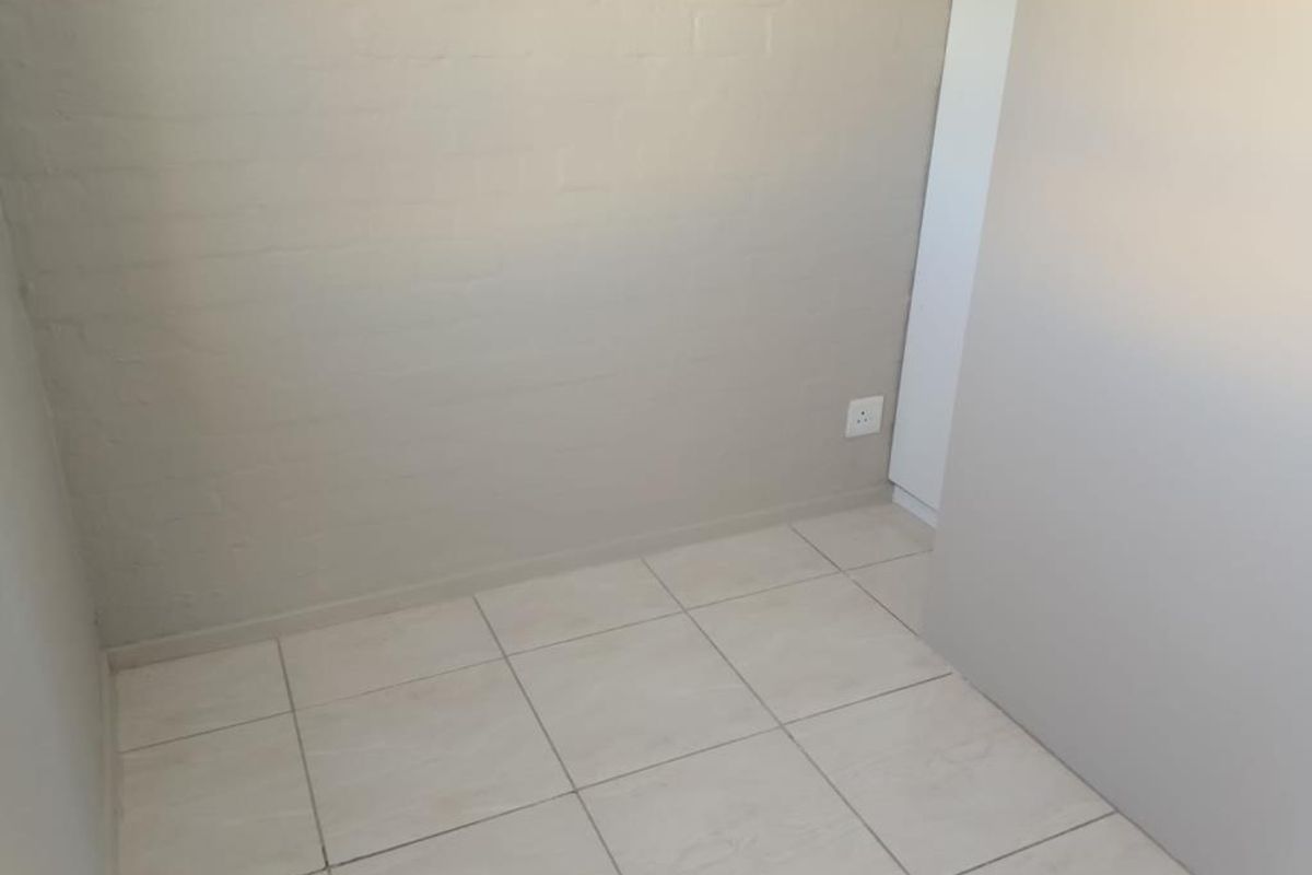 A simple, empty bedroom space featuring neutral painted brick walls and light-colored floor tiles, providing a blank canvas for interior design.