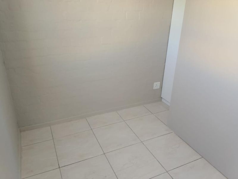 A simple, empty bedroom space featuring neutral painted brick walls and light-colored floor tiles, providing a blank canvas for interior design.