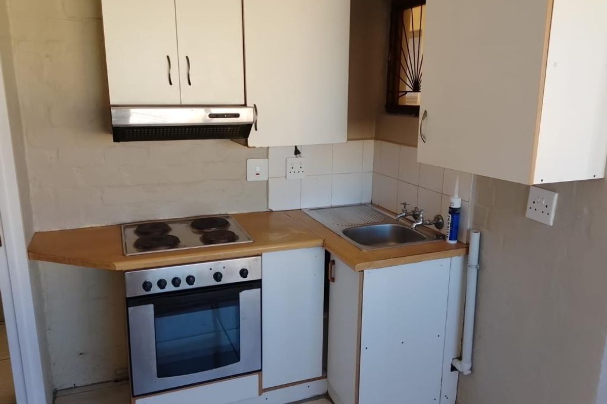 A compact kitchen featuring built-in cabinetry, an electric oven and hob, extractor fan, and a stainless steel sink with tiled splashback.