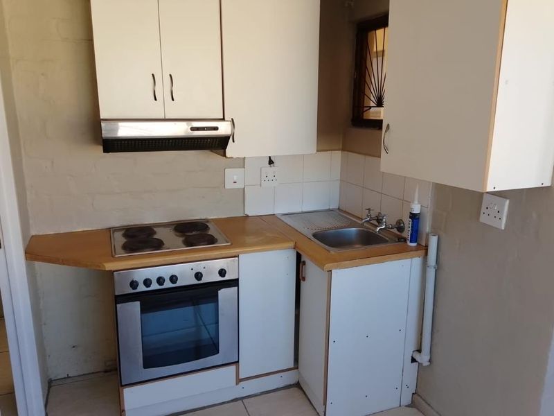 A compact kitchen featuring built-in cabinetry, an electric oven and hob, extractor fan, and a stainless steel sink with tiled splashback.