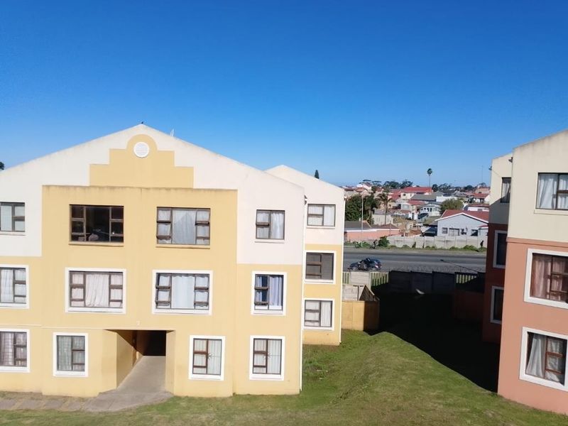 Exterior view of a multi-story apartment complex featuring yellow and peach facade finishes with aluminium window frames and surrounding communal grounds.