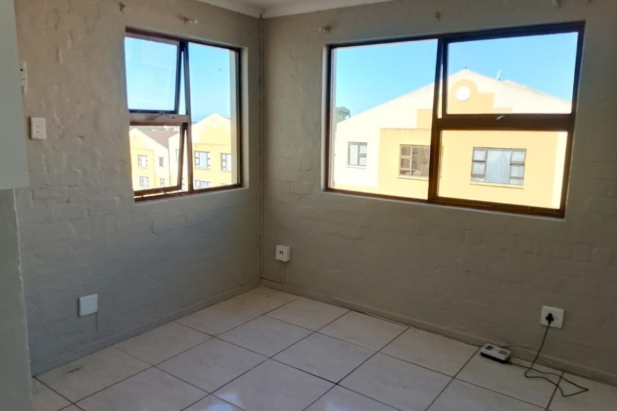 An empty living area featuring tiled flooring, painted brick walls, and large aluminium-framed windows providing natural light.