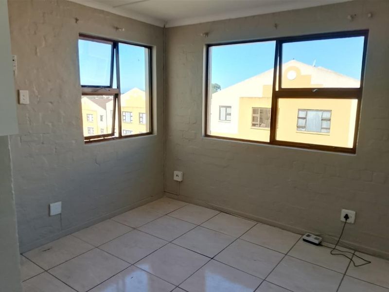 An empty living area featuring tiled flooring, painted brick walls, and large aluminium-framed windows providing natural light.