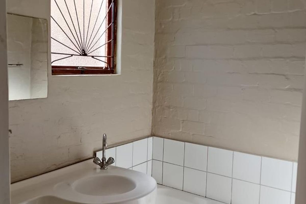 A compact bathroom featuring a bathtub and basin with tiled splashbacks, requiring cosmetic updates and repairs to the bathtub panel.