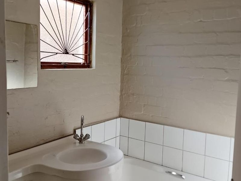A compact bathroom featuring a bathtub and basin with tiled splashbacks, requiring cosmetic updates and repairs to the bathtub panel.
