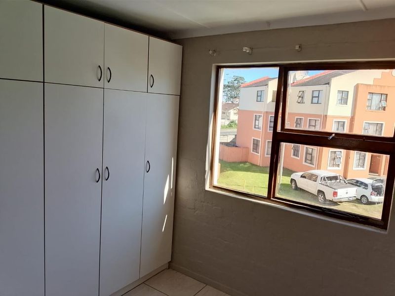 A bedroom featuring built-in cupboards and a window with views of the surrounding apartment complex.