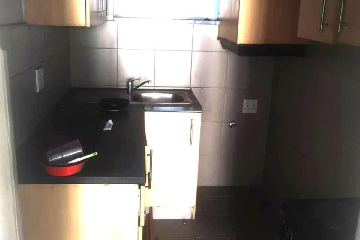 A compact kitchen featuring laminate cabinetry, a stainless steel sink, tiled backsplash, and dark floor tiles, offering potential for a modern renovation.
