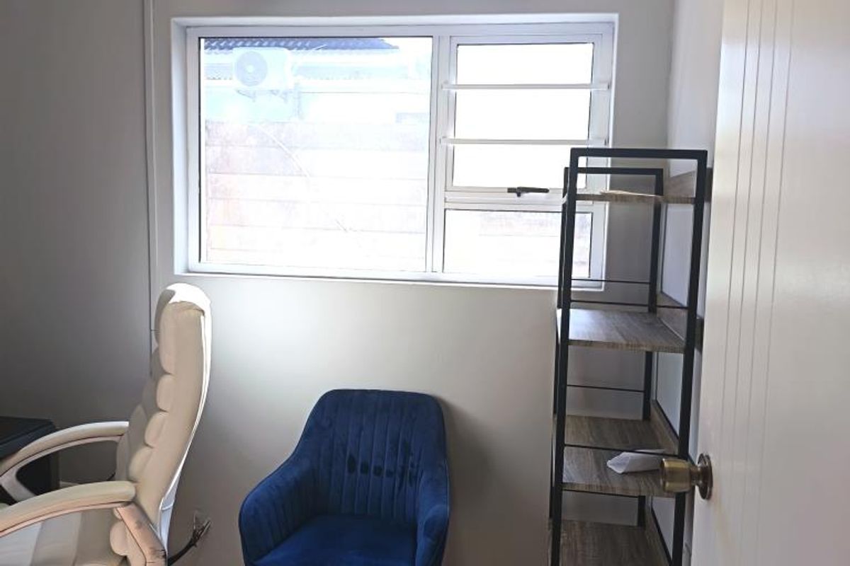 A functional office space featuring tiled flooring, a wall-mounted split-system air conditioner, and an aluminium-framed window providing natural light.