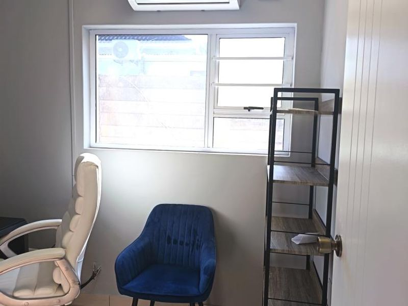 A functional office space featuring tiled flooring, a wall-mounted split-system air conditioner, and an aluminium-framed window providing natural light.