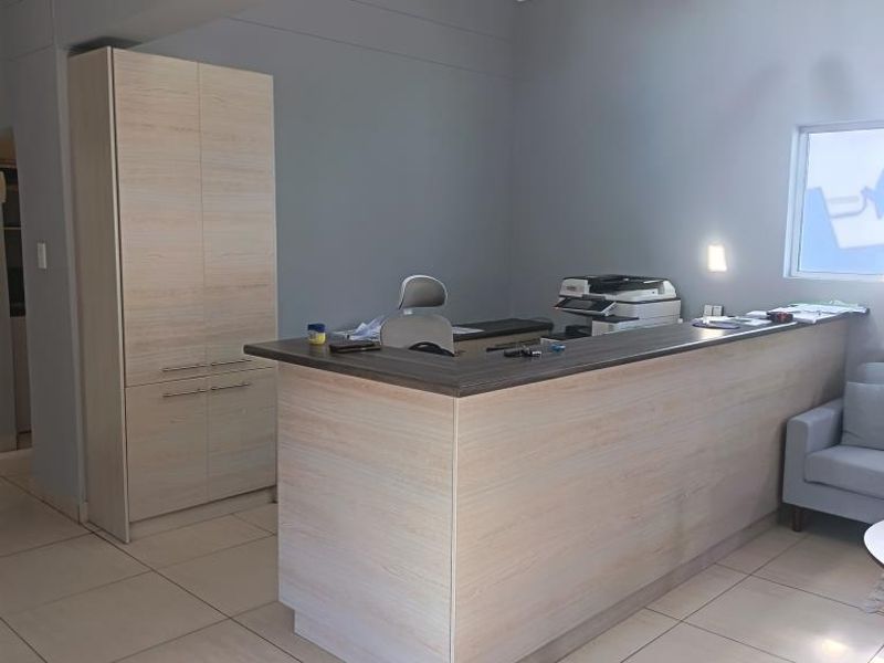 A professional commercial office space featuring a built-in reception desk, integrated storage cabinetry, and neutral tiled flooring.