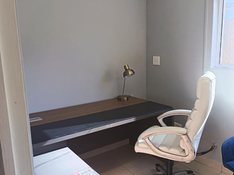 A compact, functional office space featuring tiled flooring, neutral wall finishes, and a window providing natural light.