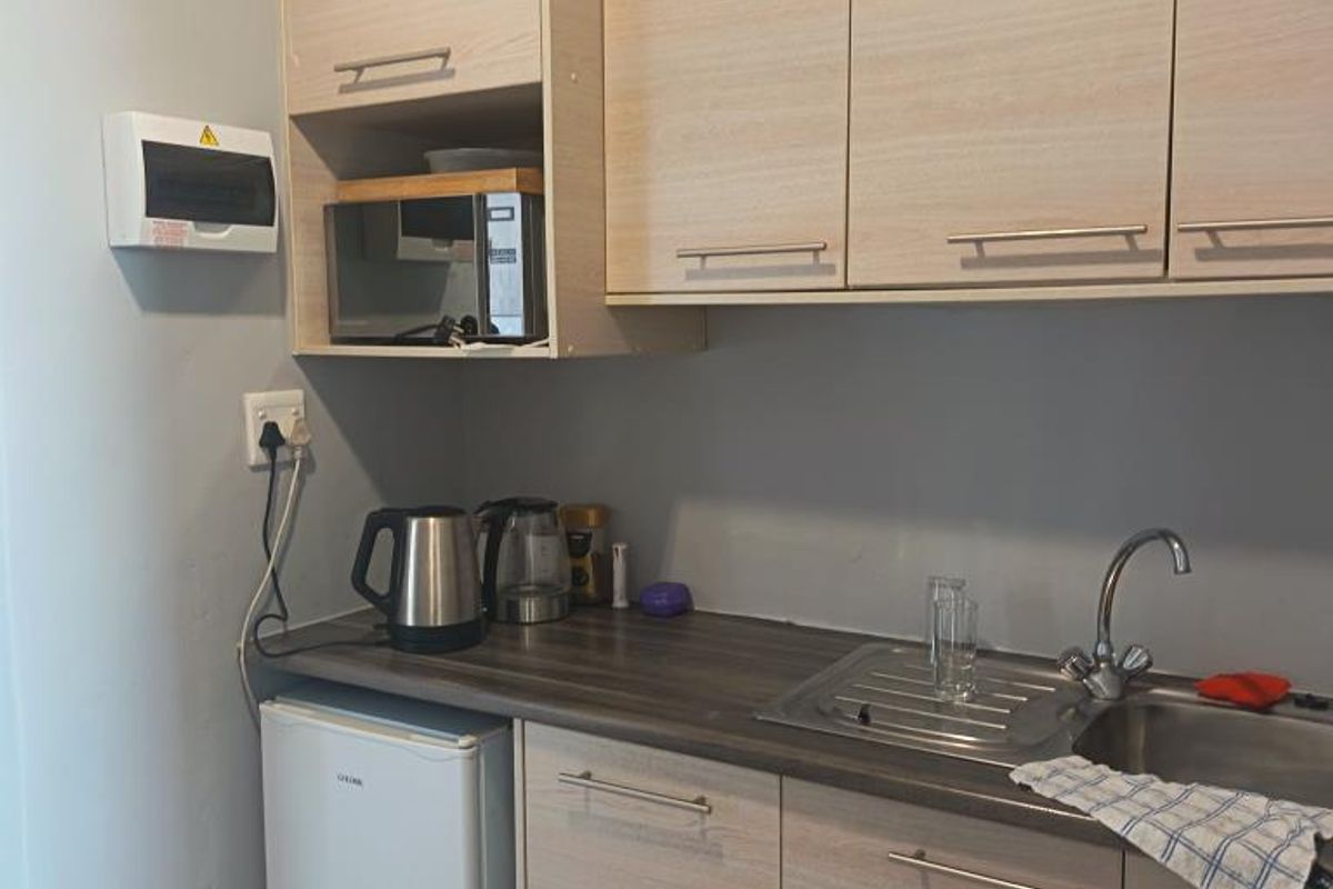 A compact kitchenette featuring light wood-finish cabinetry, a stainless steel sink, and a functional countertop area with an integrated electrical distribution board.