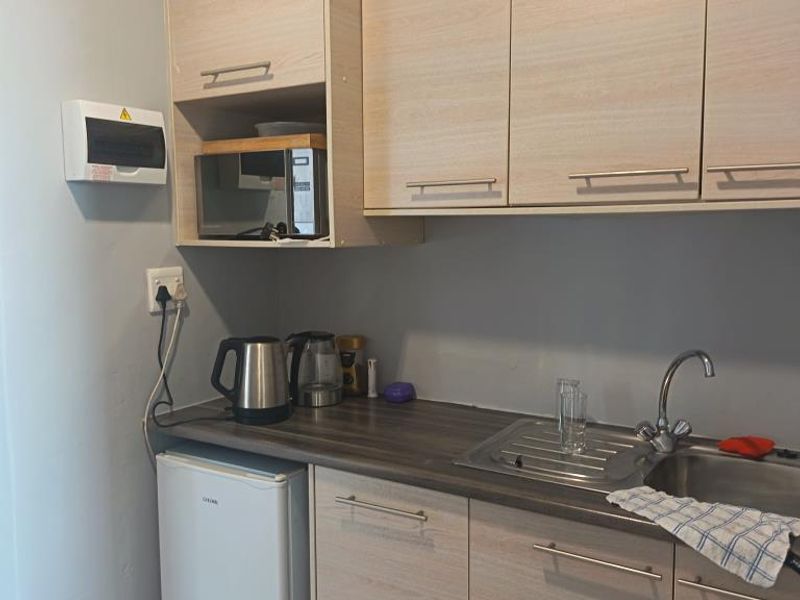 A compact kitchenette featuring light wood-finish cabinetry, a stainless steel sink, and a functional countertop area with an integrated electrical distribution board.
