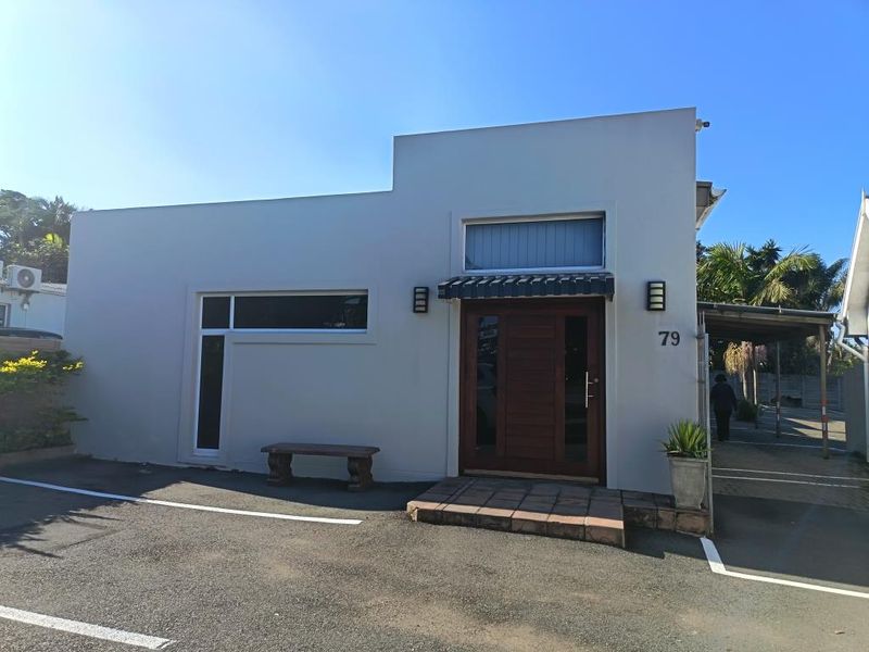 Front facade of a commercial property featuring a modern timber entrance door, tiled step, and paved parking area.