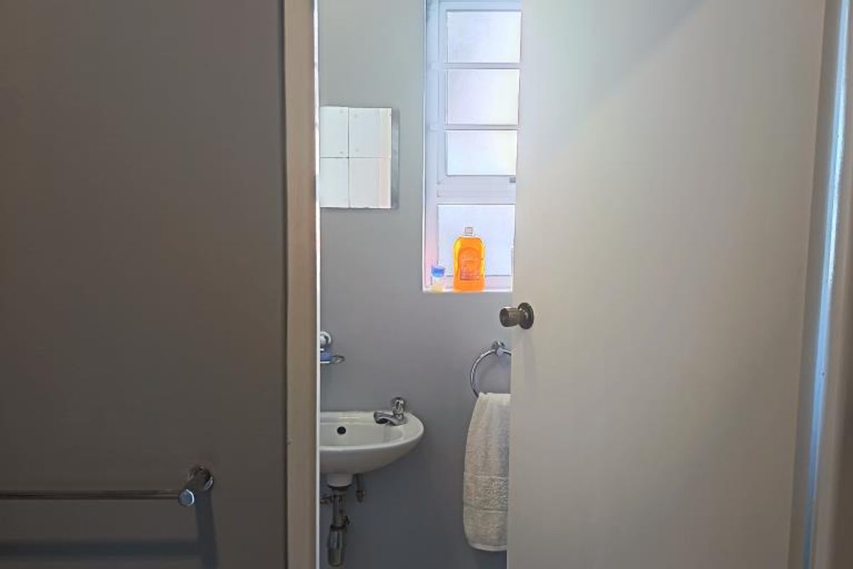 A compact bathroom featuring a pedestal basin, tiled flooring, and neutral wall finishes, viewed through an open doorway.