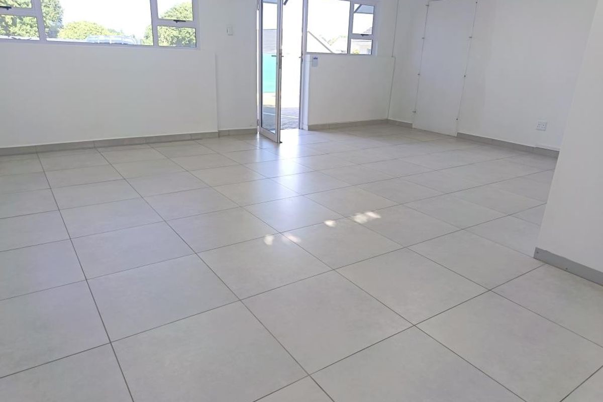 A bright, open-plan commercial office space featuring neutral tiled flooring, large windows, and direct access to an outdoor area.