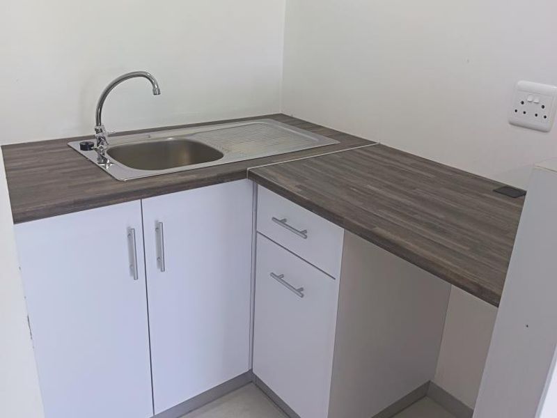 A clean and functional scullery area featuring white cabinetry, a stainless steel sink, and durable laminate countertops.