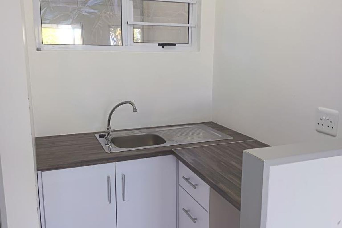 A compact, clean scullery or kitchenette area featuring white built-in cabinetry, a stainless steel sink, and a durable laminate countertop.