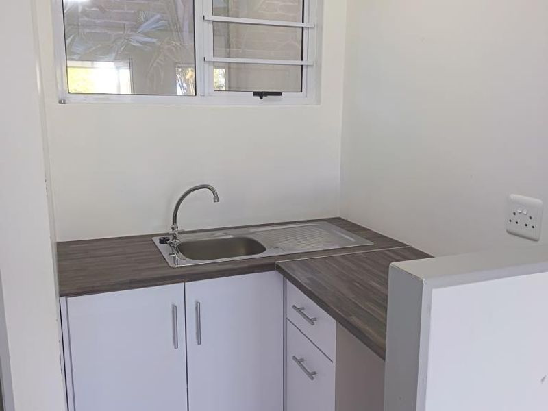 A compact, clean scullery or kitchenette area featuring white built-in cabinetry, a stainless steel sink, and a durable laminate countertop.