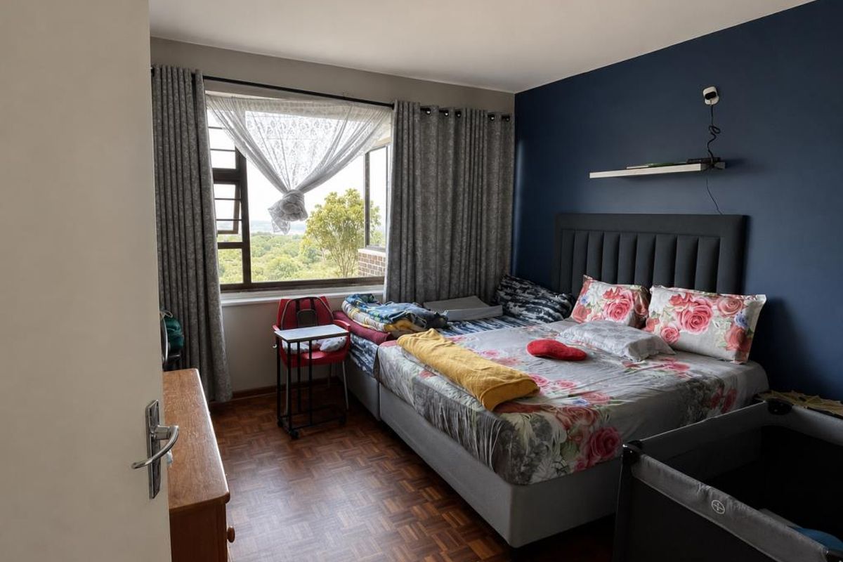 A bedroom featuring parquet flooring, a dark blue accent wall, and large windows providing natural light and exterior views.