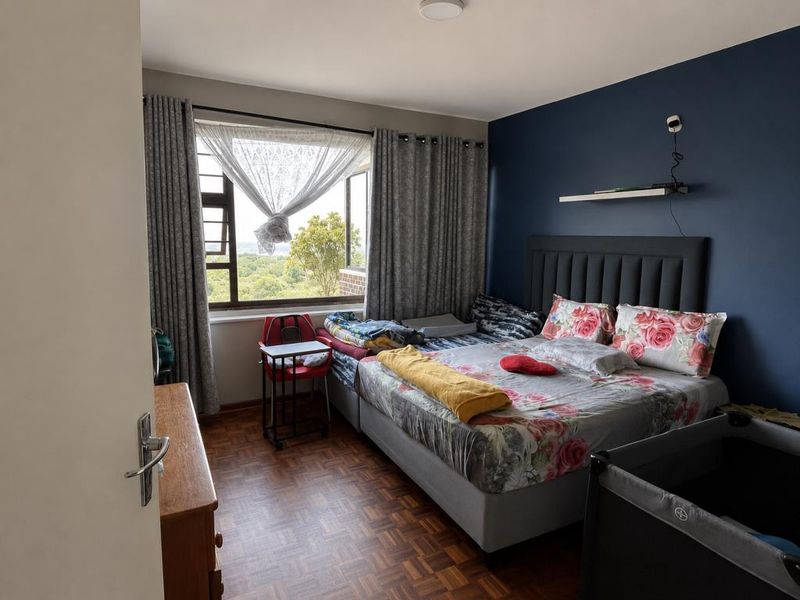A bedroom featuring parquet flooring, a dark blue accent wall, and large windows providing natural light and exterior views.