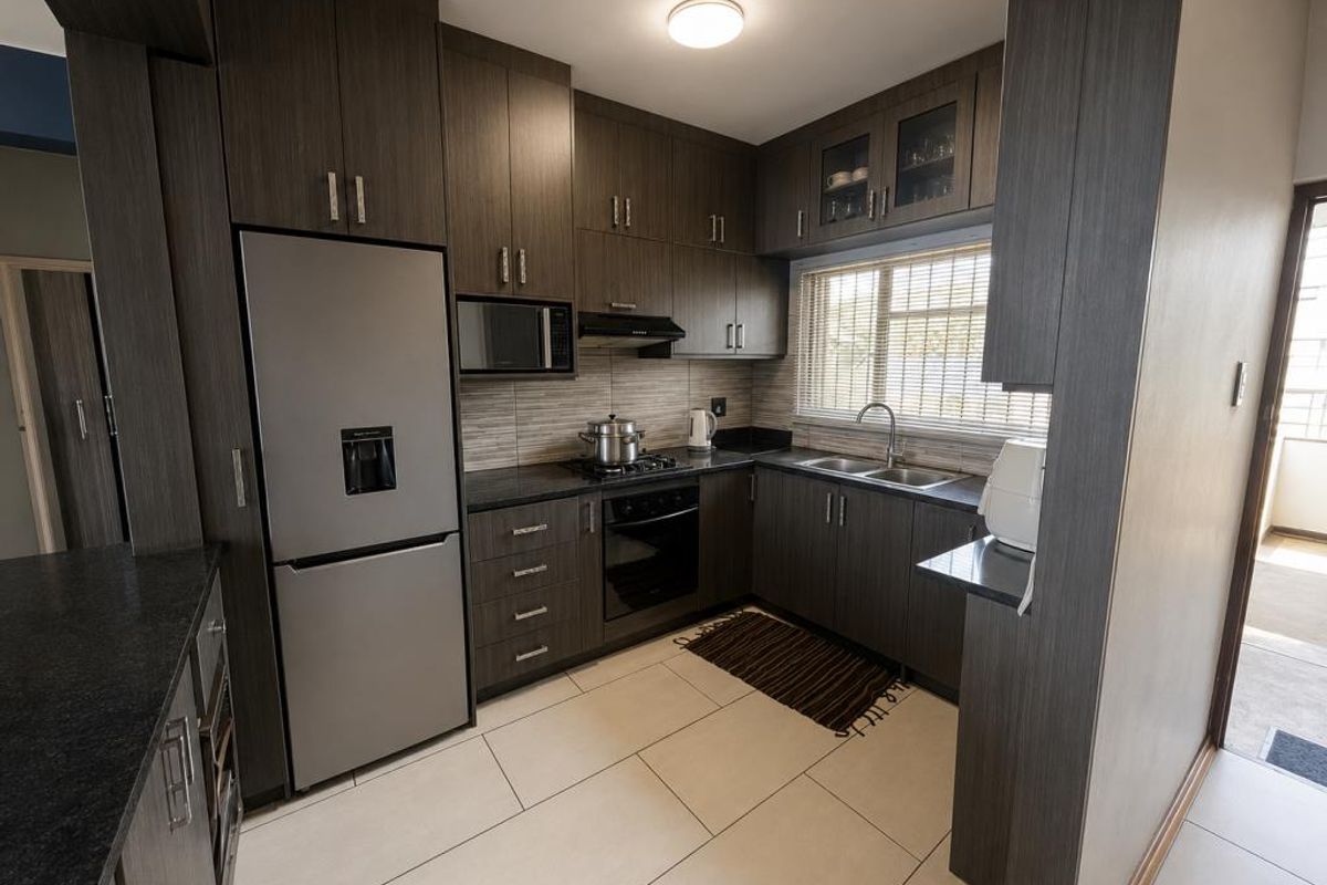 Modern kitchen featuring dark wood cabinetry, granite countertops, built-in oven, gas hob, and stainless steel sink with ample storage space.