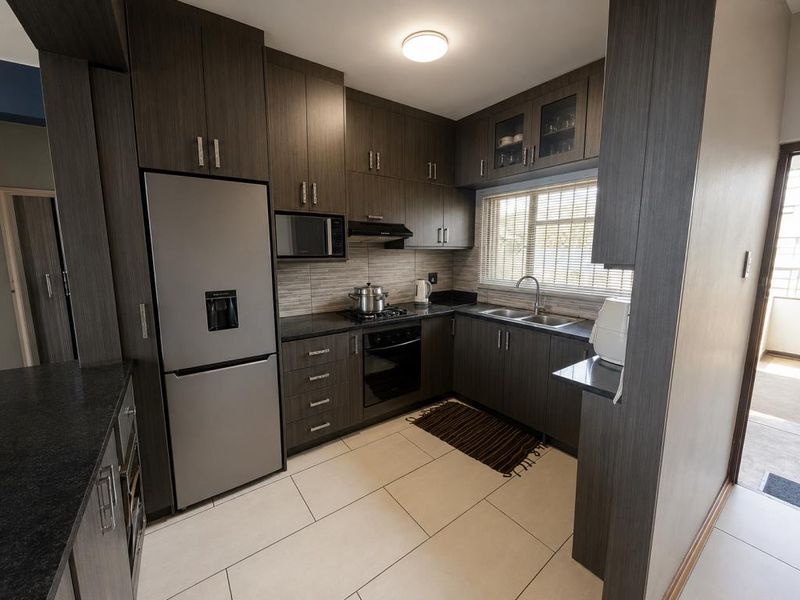 Modern kitchen featuring dark wood cabinetry, granite countertops, built-in oven, gas hob, and stainless steel sink with ample storage space.