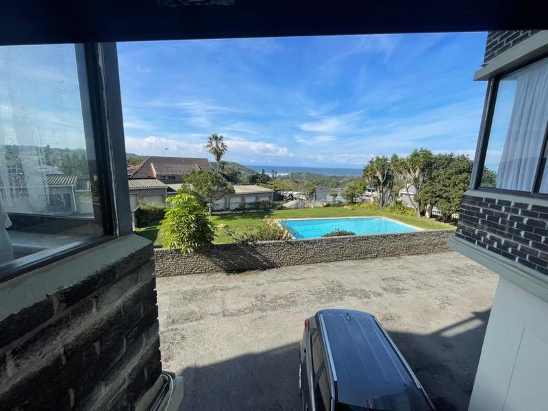 Elevated view overlooking a swimming pool, landscaped garden, and distant coastal scenery from the property.
