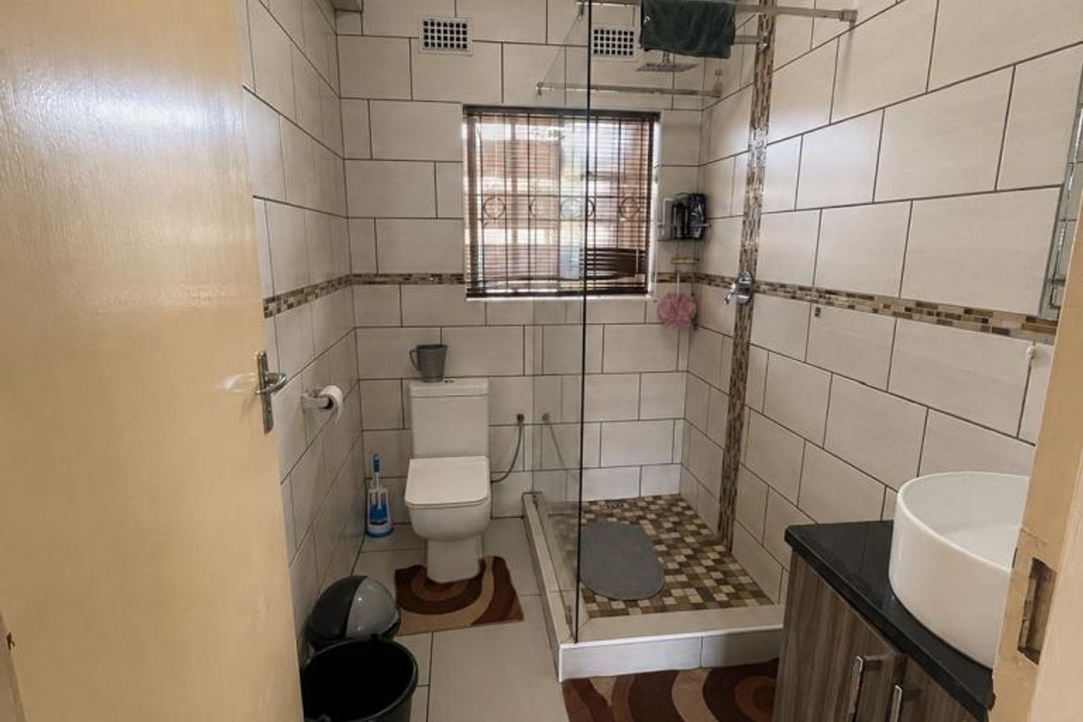 A modern bathroom featuring a walk-in shower with glass screen, a vanity cabinet with a vessel sink, and neutral wall and floor tiling.