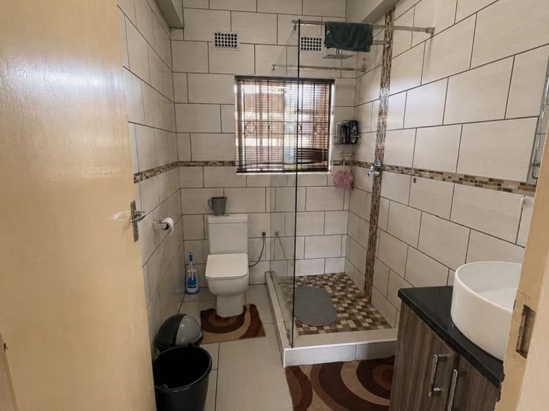 A modern bathroom featuring a walk-in shower with glass screen, a vanity cabinet with a vessel sink, and neutral wall and floor tiling.