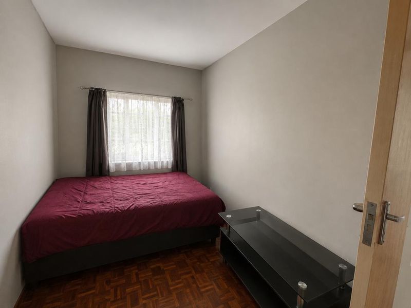 A compact bedroom featuring classic parquet flooring and neutral wall finishes, providing a functional space with natural light from the window.
