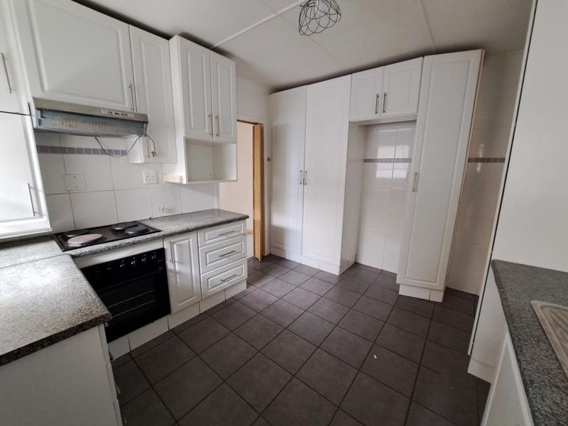 A functional kitchen featuring white built-in cabinetry, granite countertops, an integrated oven and hob, and tiled flooring throughout.