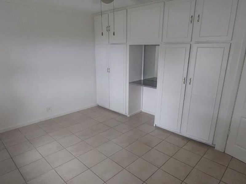 A clean, empty bedroom featuring neutral tiled flooring and extensive white built-in cabinetry with integrated storage and a small vanity area.