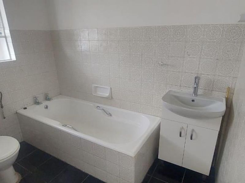 A functional bathroom featuring a bathtub, toilet, and a vanity unit with a washbasin, finished with classic wall tiling.