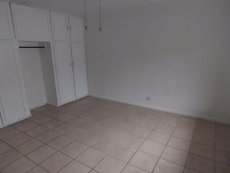 A vacant bedroom featuring neutral tiled flooring and extensive white built-in cupboard storage.