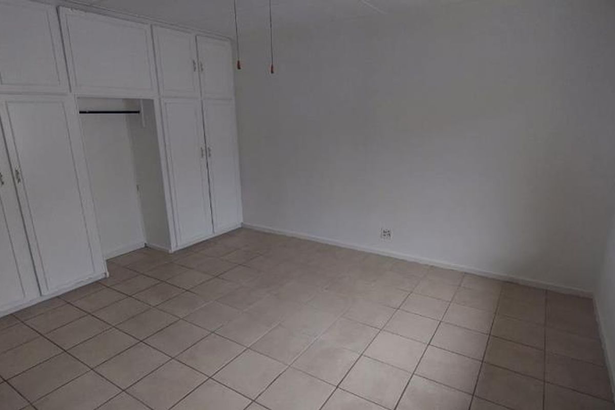 A vacant bedroom featuring neutral tiled flooring and extensive white built-in cupboard storage.