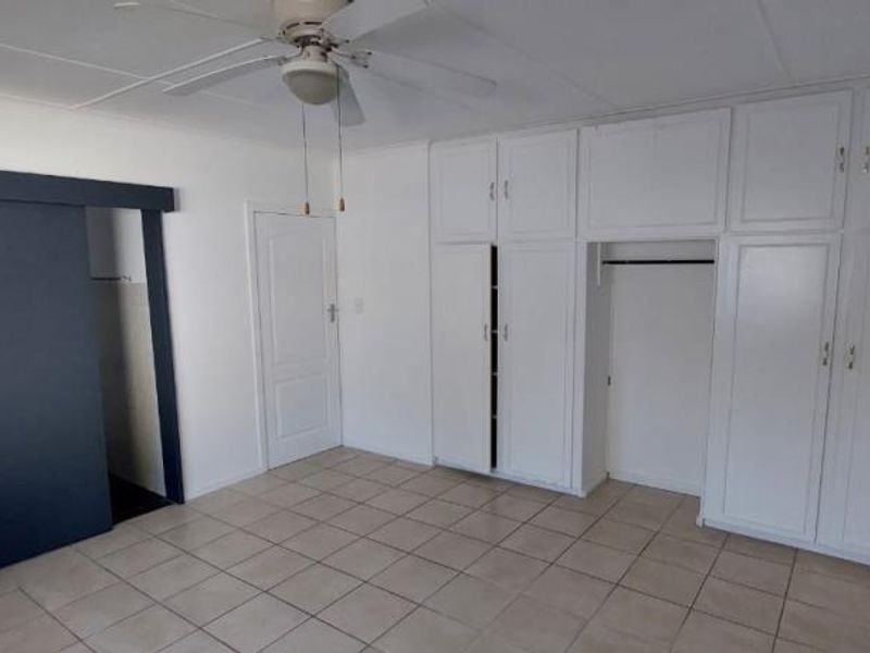 A spacious, empty bedroom featuring neutral tiled flooring, a ceiling fan, and extensive built-in storage cupboards.
