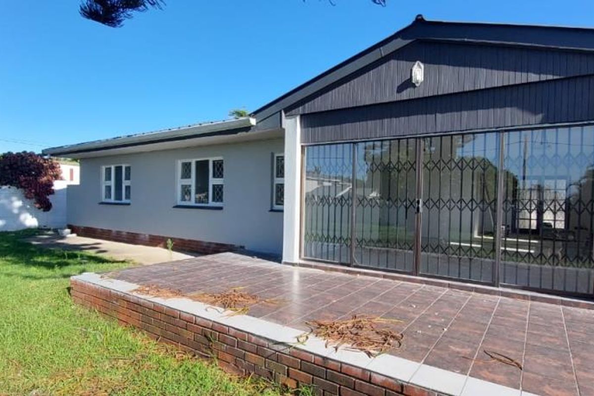 Rear view of the house featuring a tiled patio area, sliding glass doors with security gates, and a well-maintained lawn.
