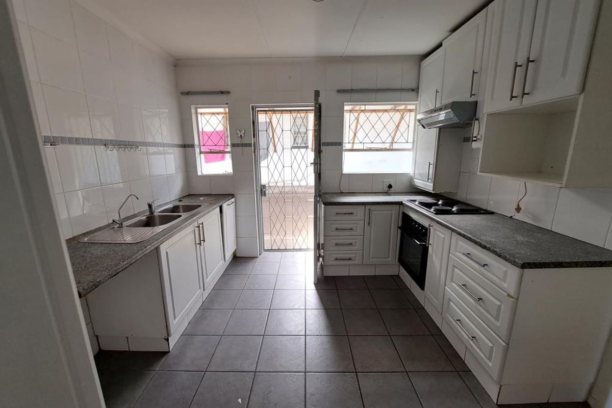 A functional kitchen featuring white cabinetry, tiled splashbacks, a double sink, and built-in cooking appliances, with direct access to the exterior.