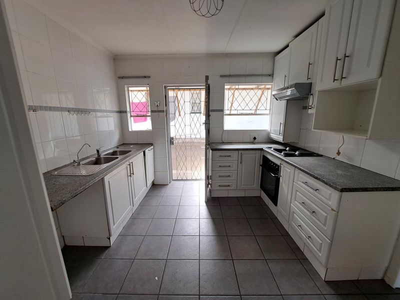 A functional kitchen featuring white cabinetry, tiled splashbacks, a double sink, and built-in cooking appliances, with direct access to the exterior.