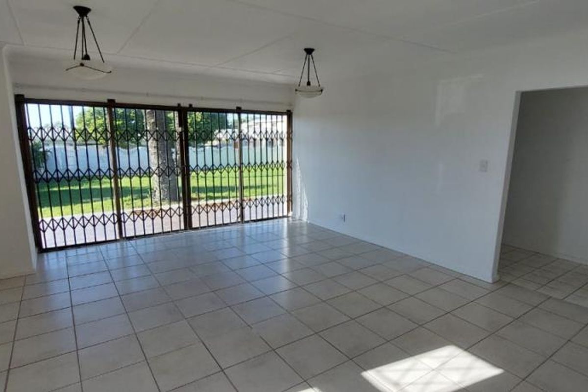 A spacious, empty living room featuring neutral tiled flooring, pendant lighting, and large sliding glass doors secured with a metal gate.