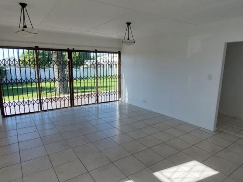 A spacious, empty living room featuring neutral tiled flooring, pendant lighting, and large sliding glass doors secured with a metal gate.