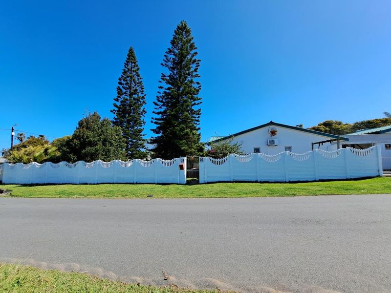 Front view of the property featuring a white decorative boundary fence, pedestrian gate, and established pine trees along the street frontage.
